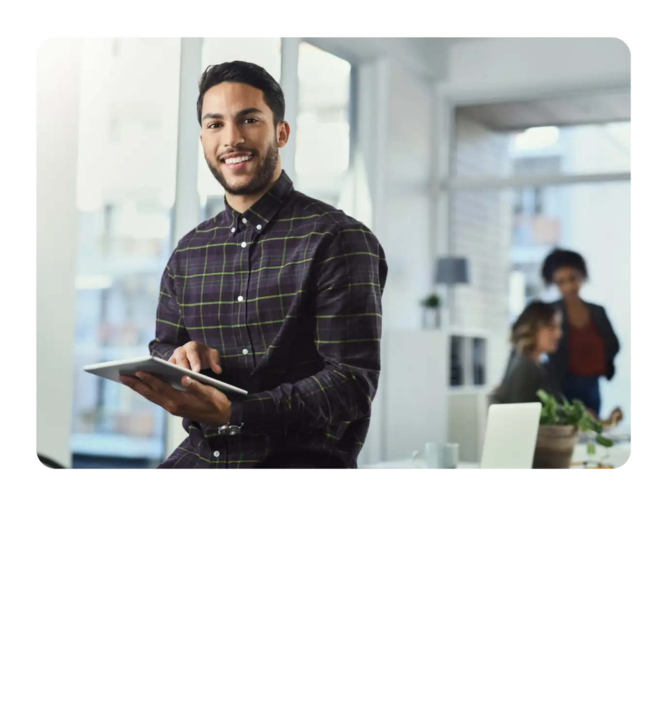 A smiling male professional holding a tablet in a modern office environment.