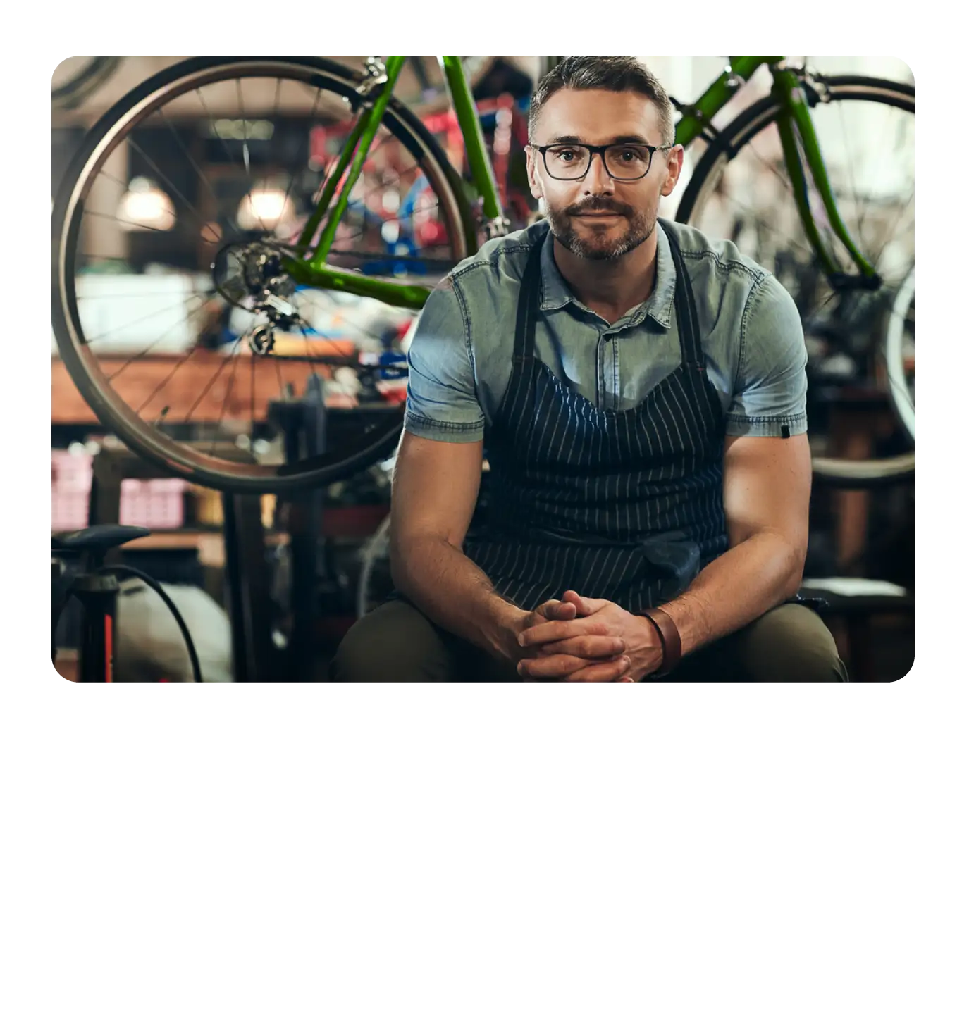 A man wearing an apron sitting confidently in a bicycle repair shop.