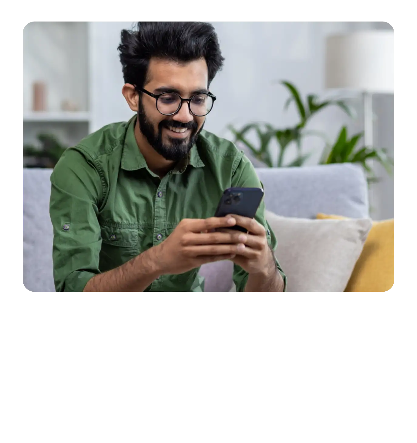 A smiling man sitting on a couch using his smartphone.
