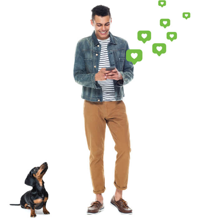 Dog looking up at a smiling young man who is checking his mobile phone