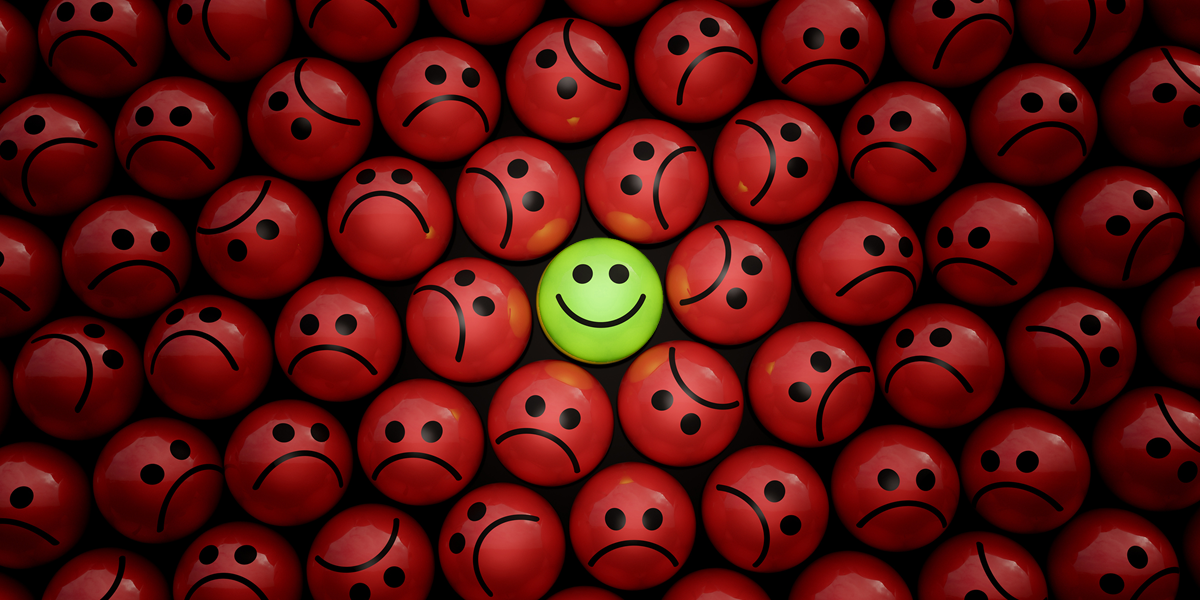 A green happy face among a pile of red sad faces